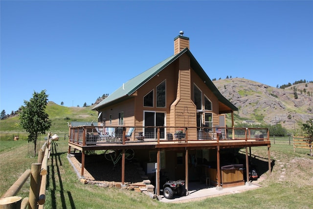 back of property featuring a rural view, a deck with mountain view, a chimney, and fence