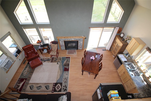 living area with high vaulted ceiling, a glass covered fireplace, plenty of natural light, and wood finished floors