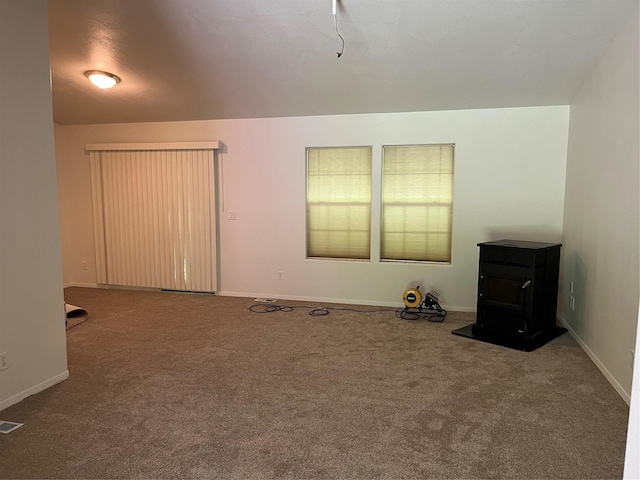 carpeted empty room with visible vents, baseboards, and a wood stove