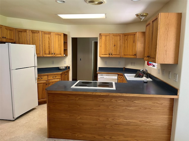 kitchen featuring dark countertops, a peninsula, white appliances, and a sink