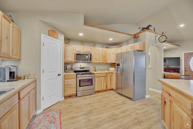 kitchen featuring light brown cabinetry, light wood-type flooring, light countertops, lofted ceiling, and stainless steel appliances