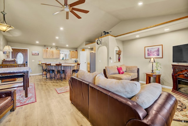 living area with bar, a ceiling fan, vaulted ceiling, baseboards, and light wood finished floors