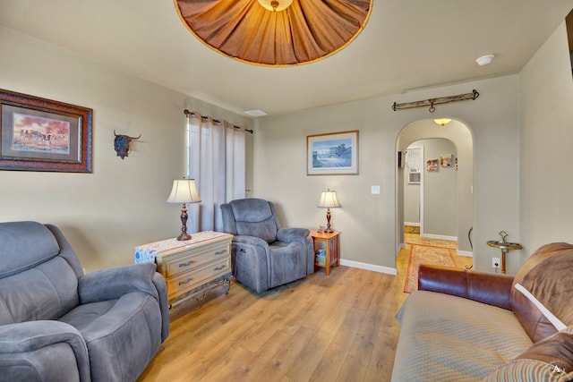 living room with arched walkways, baseboards, and light wood-type flooring