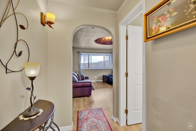 hallway featuring arched walkways, baseboards, and light wood finished floors