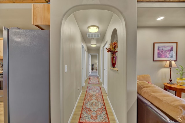 corridor featuring arched walkways, baseboards, visible vents, and light wood-type flooring