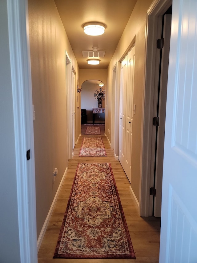 corridor featuring arched walkways, baseboards, and light wood-style floors