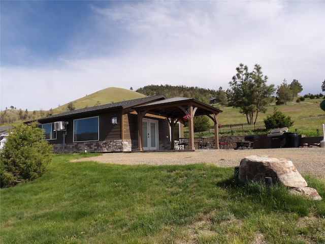 rear view of property featuring french doors, a lawn, and stone siding