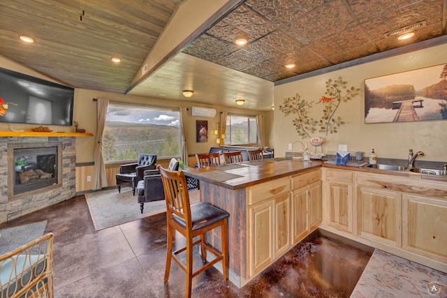 kitchen with a peninsula, light brown cabinets, a fireplace, a wall mounted air conditioner, and a sink