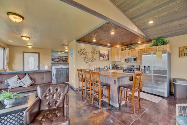 kitchen featuring a peninsula, light brown cabinets, baseboards, finished concrete floors, and appliances with stainless steel finishes