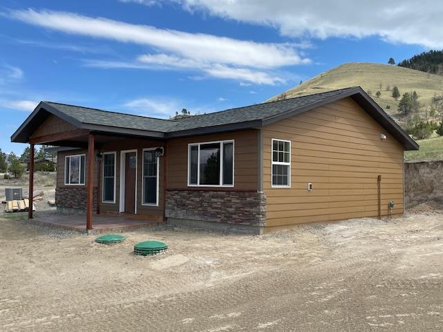 rear view of property with central AC, a shingled roof, a mountain view, and stone siding