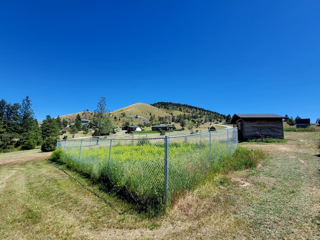 view of yard featuring fence, a mountain view, an outdoor structure, and a rural view