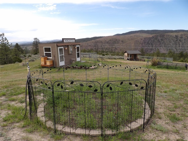 view of gate with an outdoor structure, fence, a rural view, a mountain view, and a yard