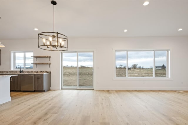 interior space featuring light stone countertops, light wood-type flooring, stainless steel dishwasher, pendant lighting, and a chandelier