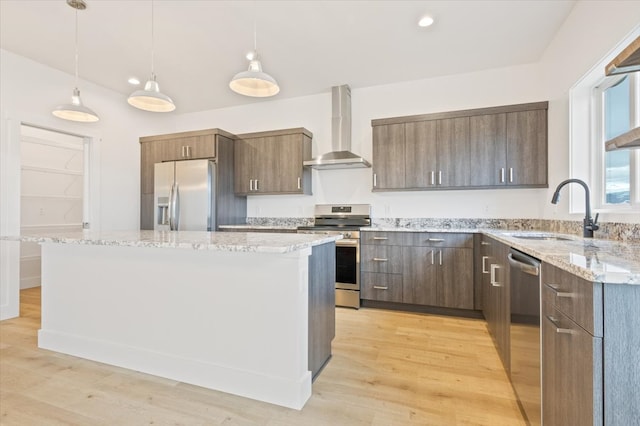 kitchen featuring sink, wall chimney range hood, appliances with stainless steel finishes, a kitchen island, and light wood-type flooring