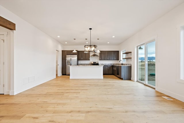 kitchen with pendant lighting, a center island, wall chimney exhaust hood, light wood-type flooring, and appliances with stainless steel finishes