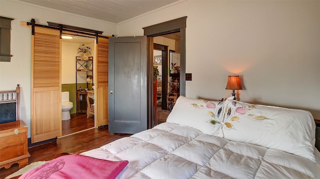 bedroom with crown molding, connected bathroom, dark hardwood / wood-style floors, and a barn door