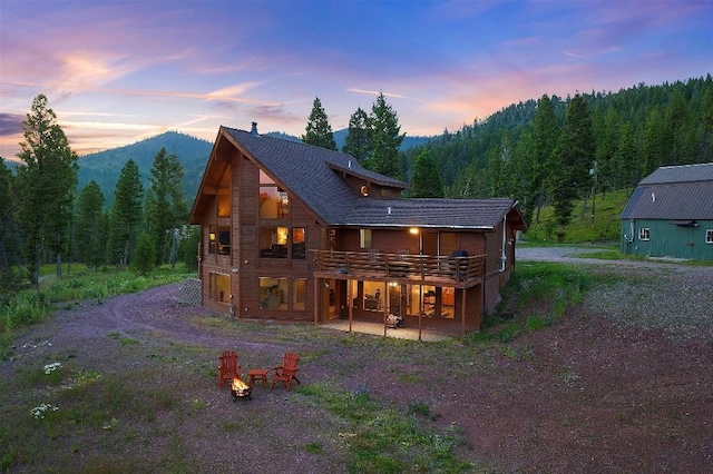 back of house at dusk featuring a patio area, a mountain view, a view of trees, driveway, and a fire pit