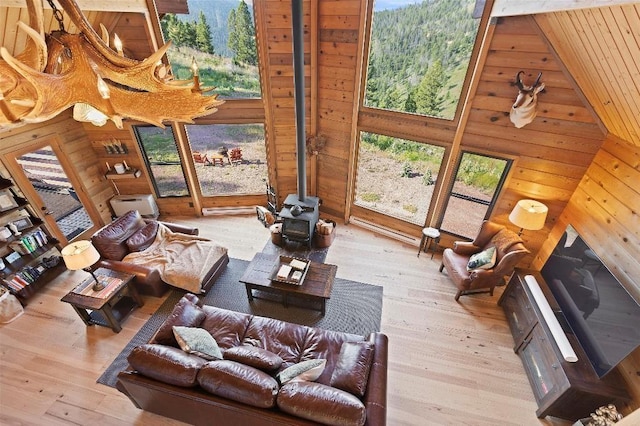 living area featuring light wood-type flooring, a towering ceiling, a wood stove, and wooden walls