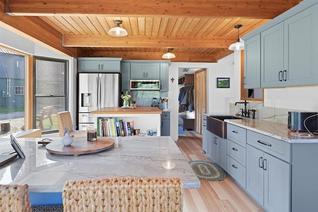 kitchen with hanging light fixtures, appliances with stainless steel finishes, a sink, and light stone counters