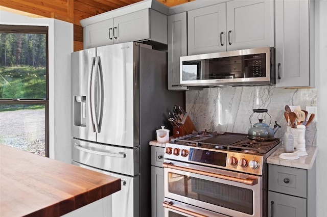 kitchen with tasteful backsplash, stainless steel appliances, wooden counters, and gray cabinetry