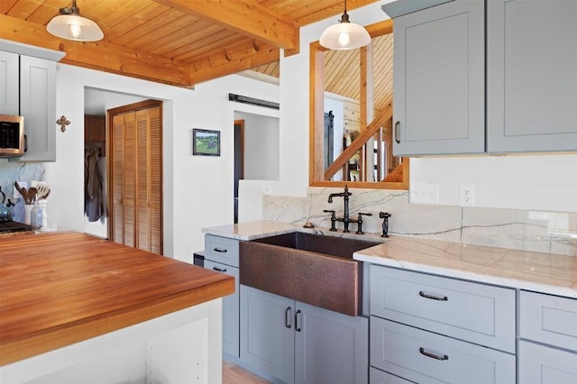 kitchen with light stone counters, pendant lighting, beam ceiling, a barn door, and wood ceiling