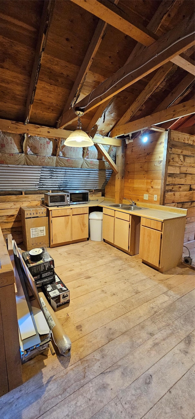 kitchen featuring light wood-style flooring, vaulted ceiling with beams, light countertops, wood walls, and a sink