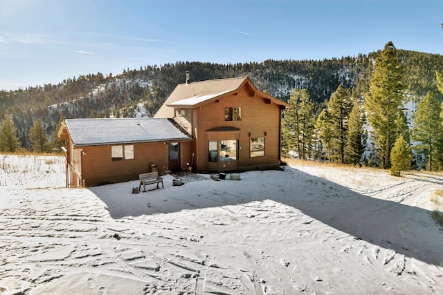 snow covered rear of property featuring a view of trees