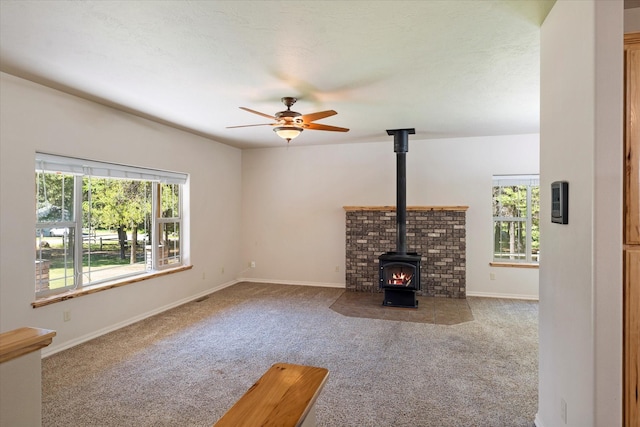 unfurnished living room featuring a wood stove, ceiling fan, and carpet floors