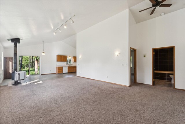 unfurnished living room with a wood stove, ceiling fan, carpet, rail lighting, and high vaulted ceiling