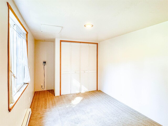 unfurnished bedroom featuring a baseboard heating unit, multiple windows, carpet flooring, and a closet