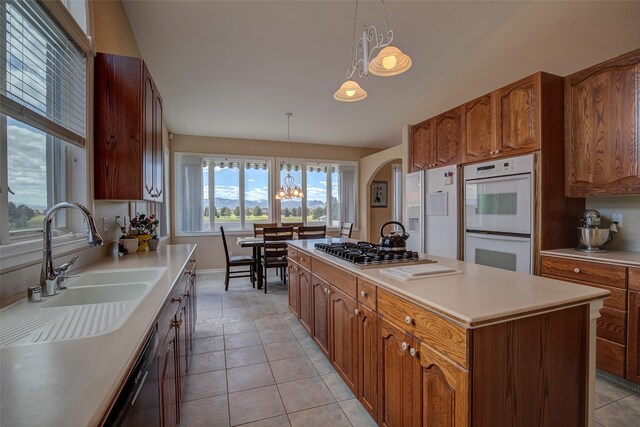 kitchen featuring sink, decorative light fixtures, double oven, a kitchen island, and stainless steel gas stovetop