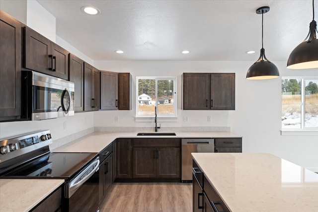 kitchen featuring sink, pendant lighting, dark brown cabinets, appliances with stainless steel finishes, and light wood-type flooring