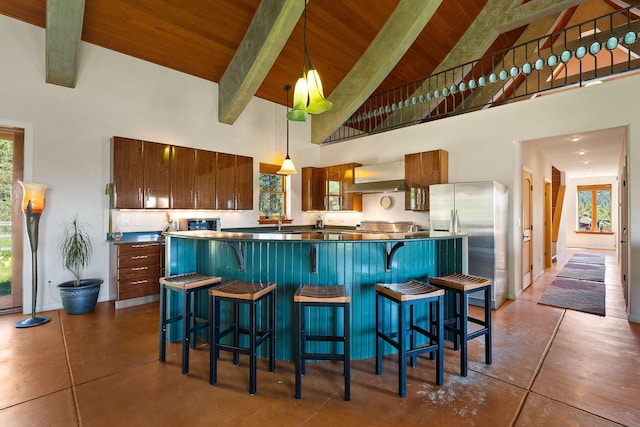 kitchen with high vaulted ceiling, decorative light fixtures, wall chimney exhaust hood, and stainless steel fridge