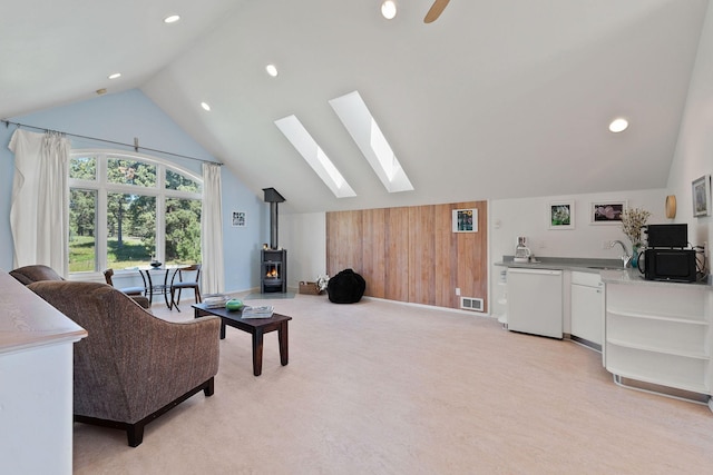 sitting room with wooden walls, a wood stove, sink, ceiling fan, and lofted ceiling with skylight