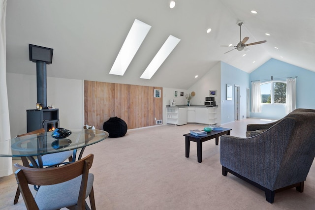 living room with ceiling fan, light colored carpet, vaulted ceiling with skylight, and a wood stove