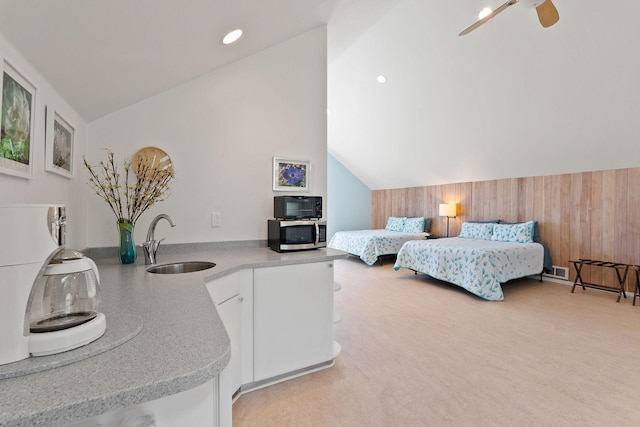 carpeted bedroom featuring vaulted ceiling, ceiling fan, wood walls, and sink