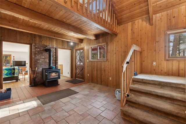 foyer with wood ceiling, stairway, a wood stove, wood walls, and beam ceiling