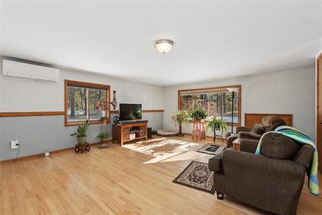 living area featuring a wealth of natural light, baseboards, a wall unit AC, and light wood finished floors