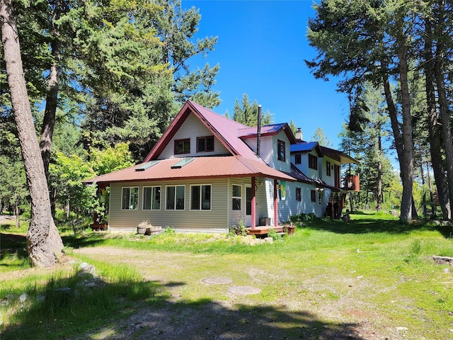 rear view of house featuring metal roof, a lawn, and a chimney