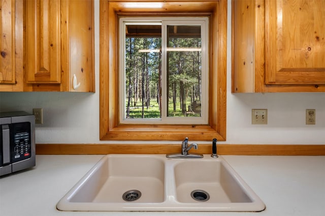 kitchen featuring a sink, brown cabinetry, light countertops, and stainless steel microwave