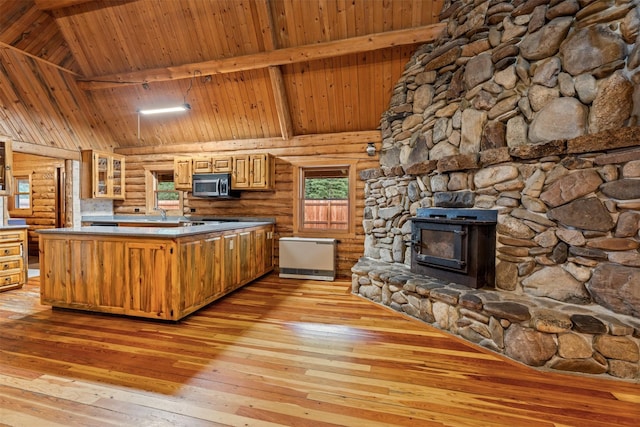 kitchen featuring stainless steel microwave, a peninsula, light wood-style floors, high vaulted ceiling, and glass insert cabinets