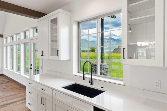 kitchen with light hardwood / wood-style flooring, white cabinetry, beamed ceiling, sink, and a mountain view