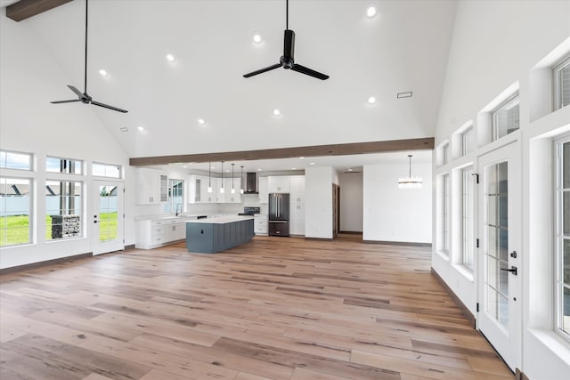 unfurnished living room with high vaulted ceiling, beamed ceiling, light hardwood / wood-style floors, and ceiling fan with notable chandelier