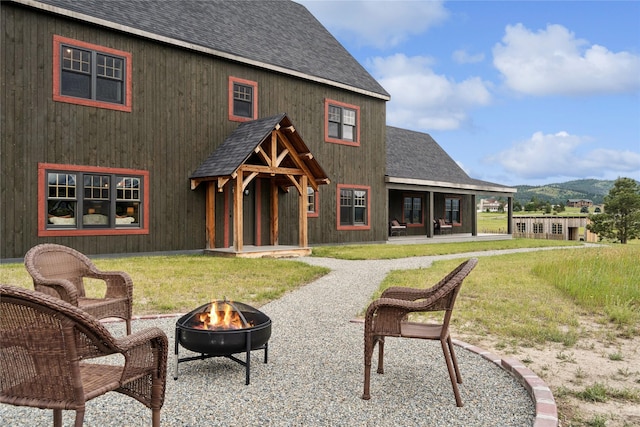 285 N Hill Rd, Kalispell, MT 59901 - rear view of house with an outdoor fire pit, roof with shingles, a lawn, a patio, and a mountain view