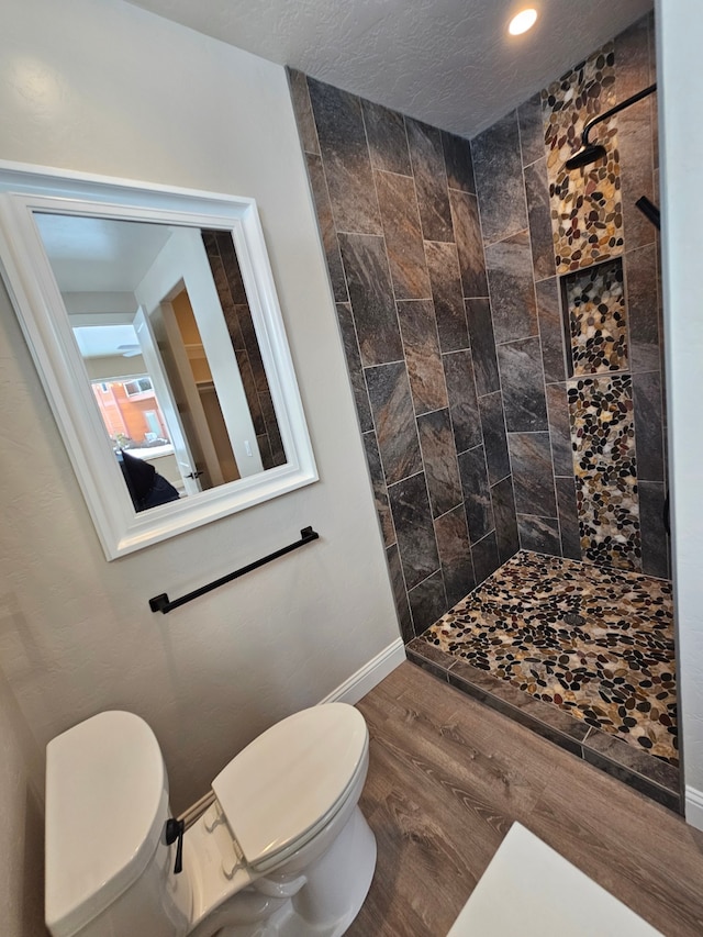 bathroom with wood-type flooring, tiled shower, a textured ceiling, and toilet