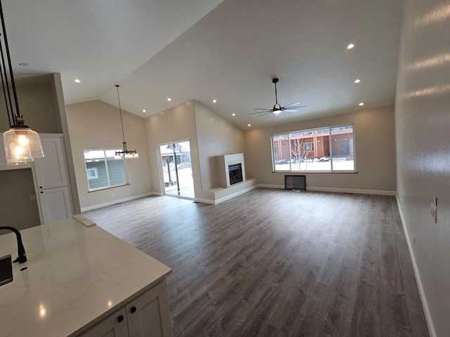 unfurnished living room featuring a wealth of natural light, dark hardwood / wood-style floors, ceiling fan, and vaulted ceiling