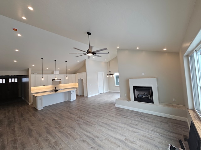 unfurnished living room featuring ceiling fan, high vaulted ceiling, sink, and light wood-type flooring