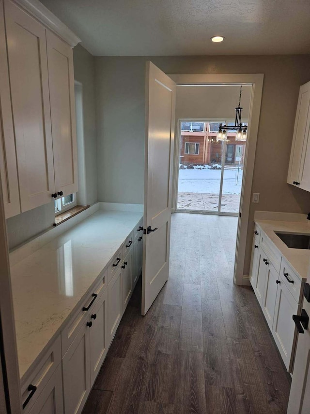 kitchen with sink, dark wood-type flooring, light stone counters, white cabinets, and decorative light fixtures