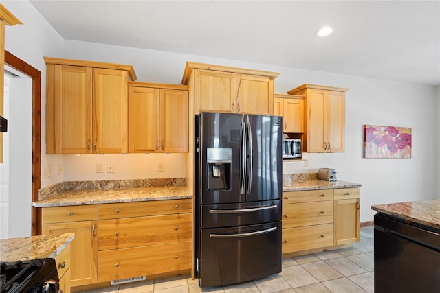 kitchen featuring light tile patterned flooring, black gas range oven, light stone counters, stainless steel refrigerator with ice dispenser, and light brown cabinets