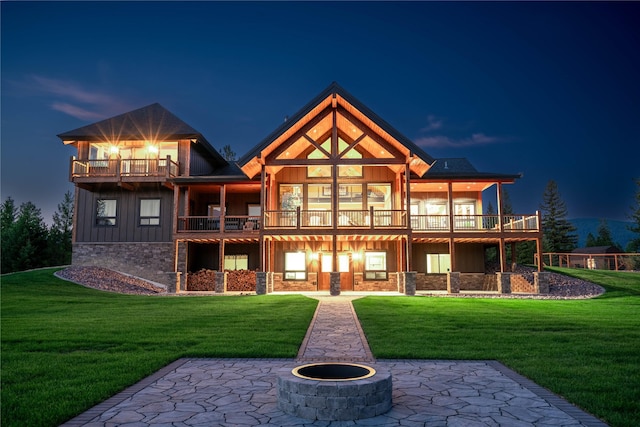 back house at dusk featuring a balcony, a lawn, a patio area, and a fire pit